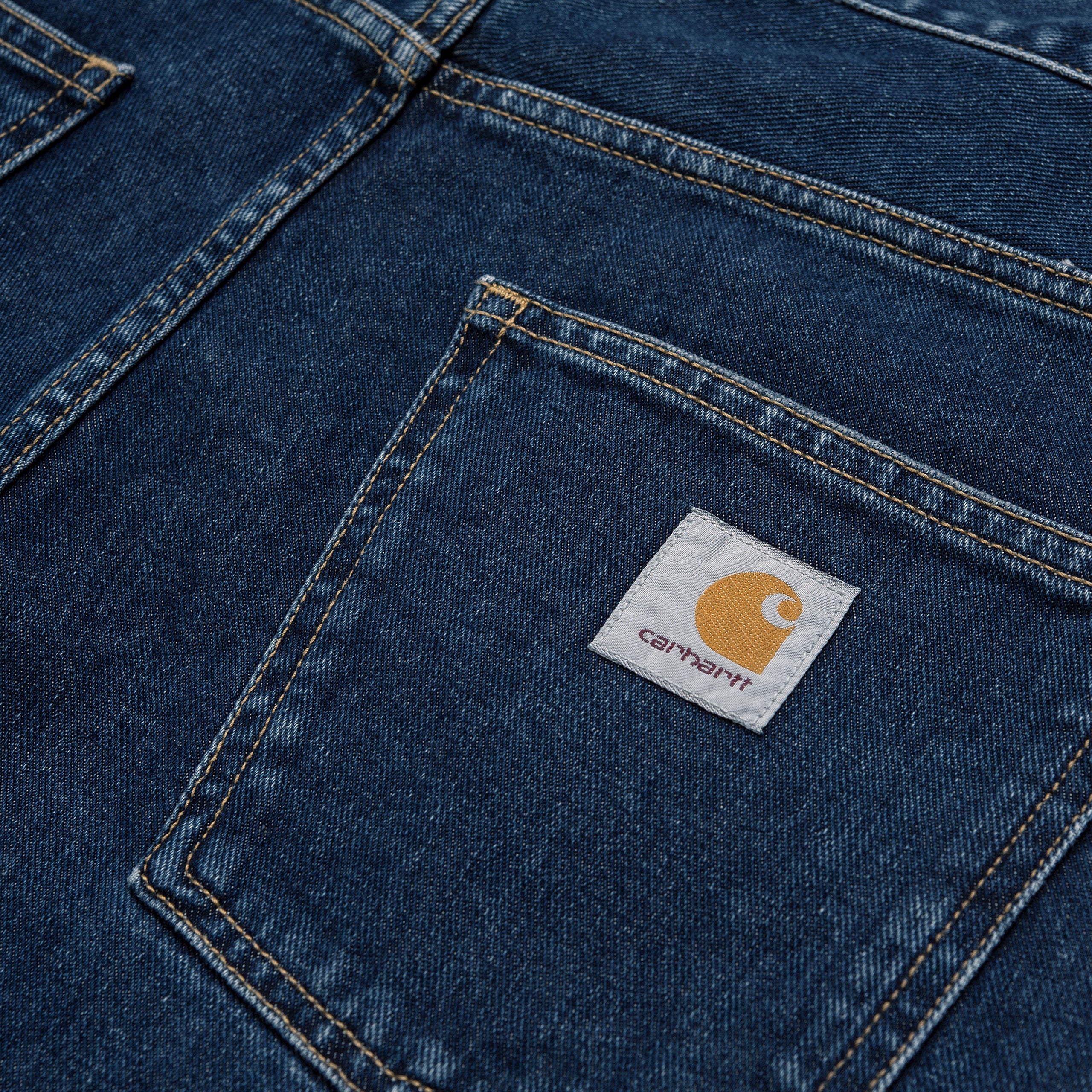 Dark blue denim Carhartt trousers with woven logo on back pocket. Free UK shipping on orders over £50.